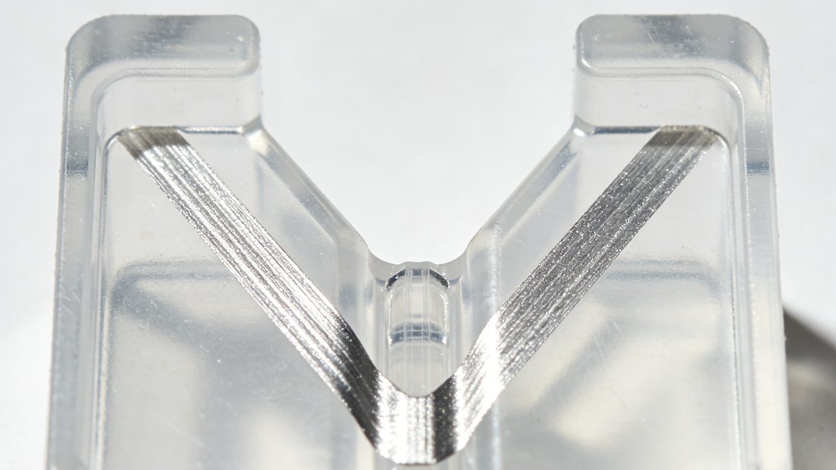 Close-up of silver streaks and splay marks on an injection molded plastic part showing V-shape pattern