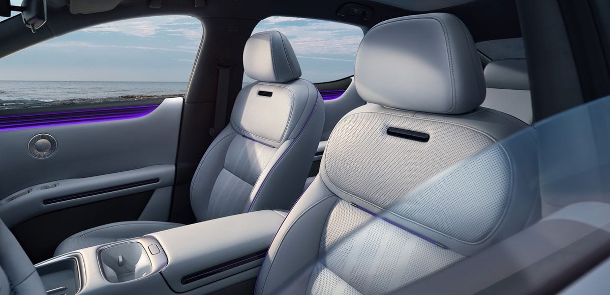 Close-up of automotive interior material layers including soft upholstery, velvet ceiling, brushed metal speaker mask, and premium plastic trim