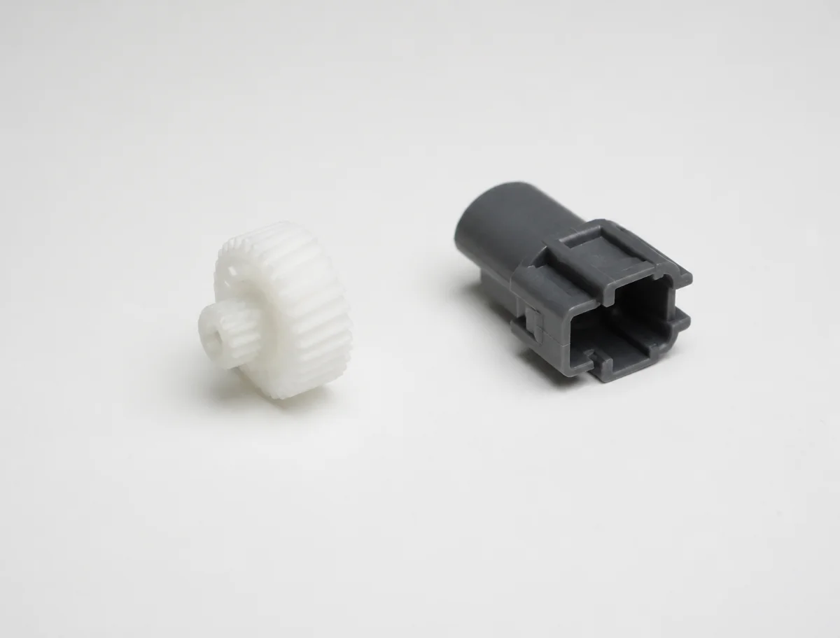 White nylon pellets and molded nylon parts, a white gear and a dark grey connector housing